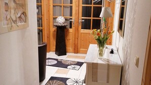 Ein Flur mit einer Holztür, einem kleinen Tisch mit Blumenvase und einem gemusterten Teppich.