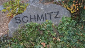 Ein mit dem Namen „SCHMITZ“ versehener Stein, umgeben von Grünpflanzen.