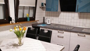Eine moderne Küche mit weißen Schränken, einer schwarzen Mikrowelle und einem blauen Backofen. Ein Esstisch mit Blumen in einer Vase und schwarzen Stühlen steht daneben.