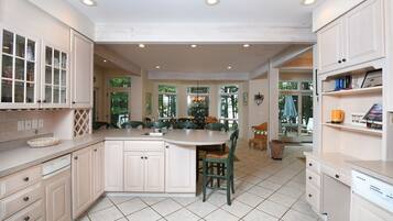A spacious kitchen with a central island, white cabinetry, and a dining area with green chairs.