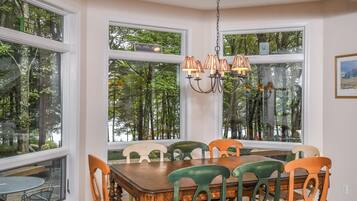 A dining area with a wooden table and chairs, large windows with a view of trees, and a chandelier.