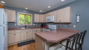 A modern kitchen with beige cabinets, a granite countertop, a built-in microwave, and a window with a view of greenery. - Grande Villa 5 Bedroom House (Oakland)