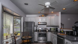 A kitchen with white cabinets, stainless steel appliances, a ceiling fan, and a dining area with chairs and a table. - Deep Creek Village 3 Bedroom Townhome #20 (McHenry)