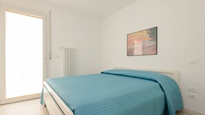 A bedroom with a bed, a radiator, a window, and a painting on the wall.