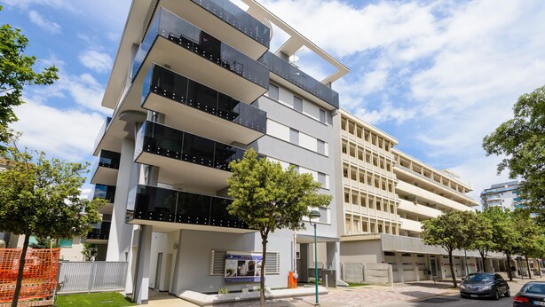 A multi-story building with balconies, a paved courtyard, and a clear sky.