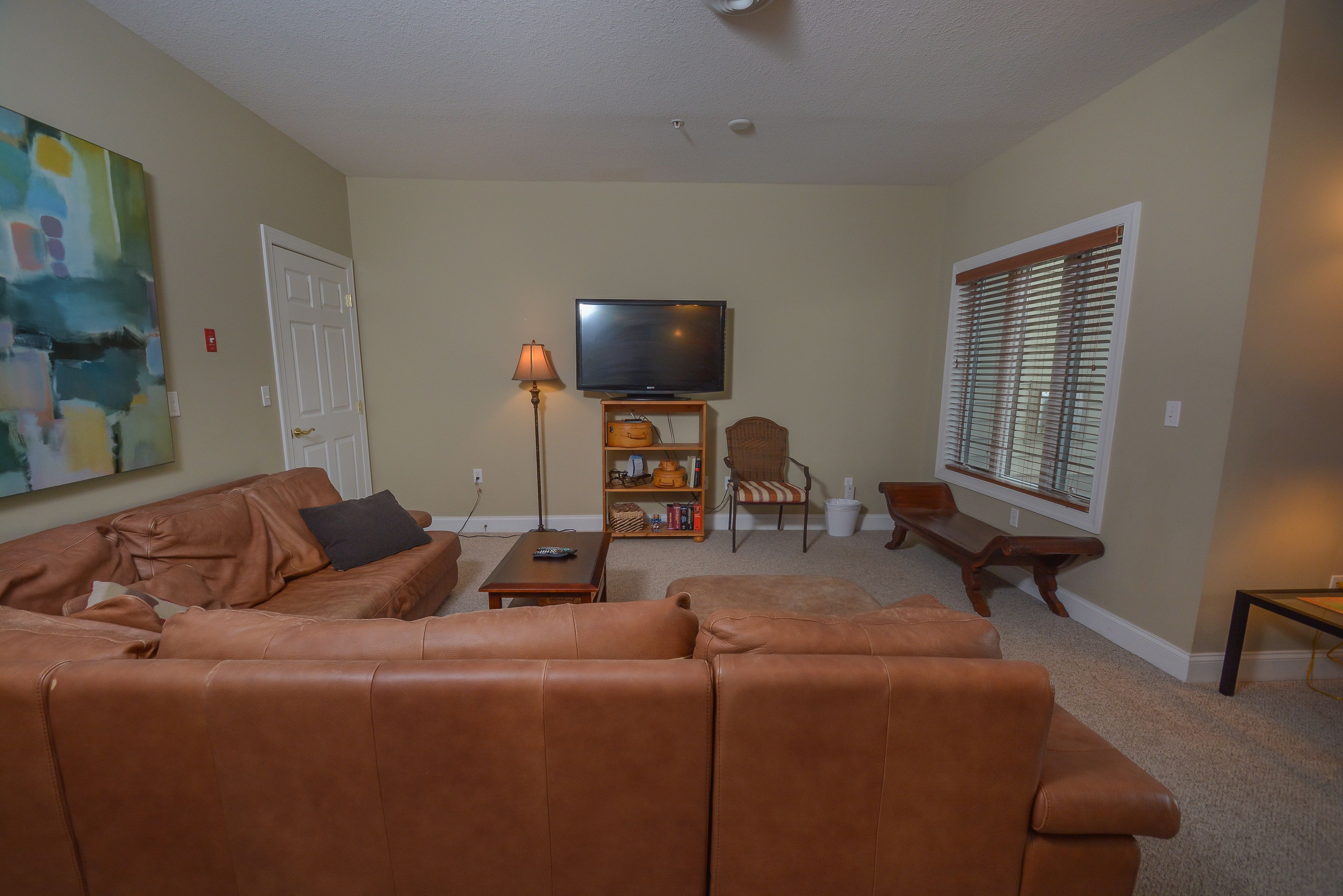 A living room with a brown leather couch, a television, a bookshelf, and a window with blinds.