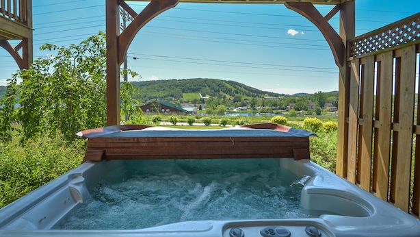 Ein Whirlpool unter einer hölzernen Pergola mit Blick auf eine grüne Landschaft und Hügel im Hintergrund.