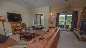 Ein Wohnzimmer mit einem Ledersofa, einem Fernseher, einer Holz-Unterhaltungseinrichtung und Blick durch eine Glastür.