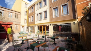 A courtyard with outdoor seating, multiple tables, and chairs, surrounded by buildings with large windows and a clear sky. - Set Ozer Hotel (Çanakkale)