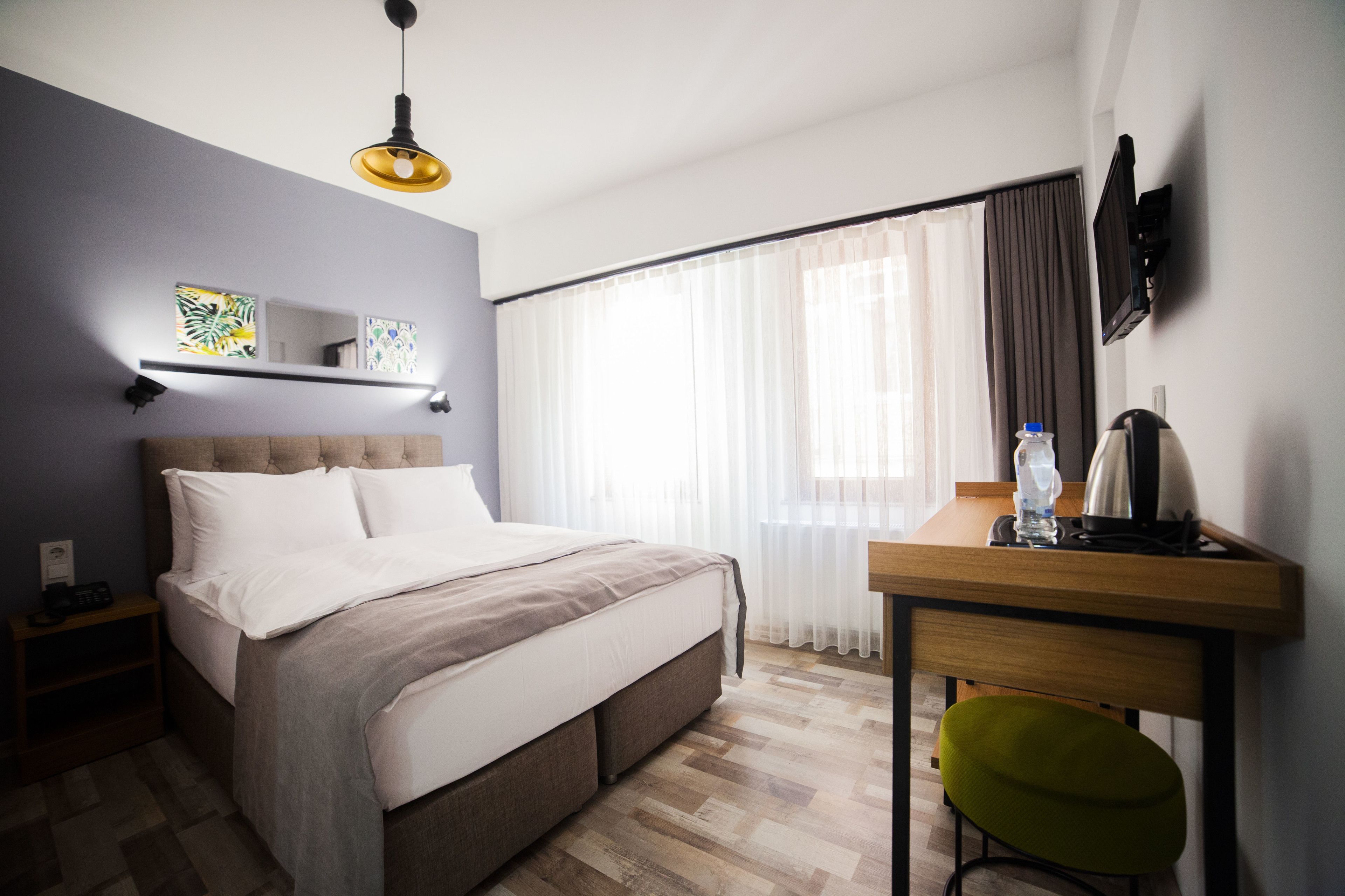 A hotel room with a bed, a desk with a chair, a TV, and a window with curtains.