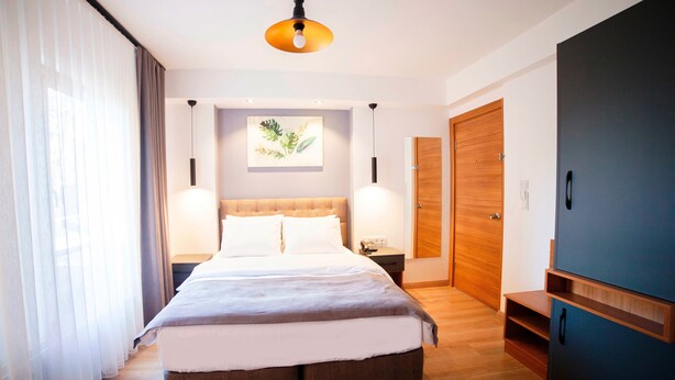 A modern hotel room with a large bed, wooden flooring, a ceiling light, a nightstand, a wall-mounted artwork, and a wardrobe. - Set Ozer Hotel (Çanakkale)