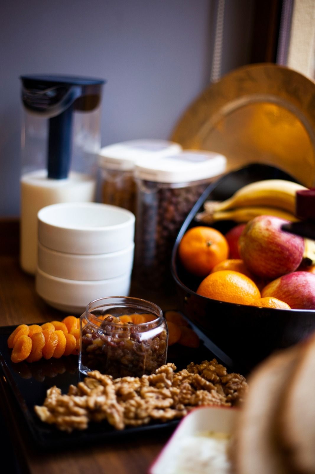 A table with a bowl of fruit, a jar of nuts, and a plate of dried apricots.