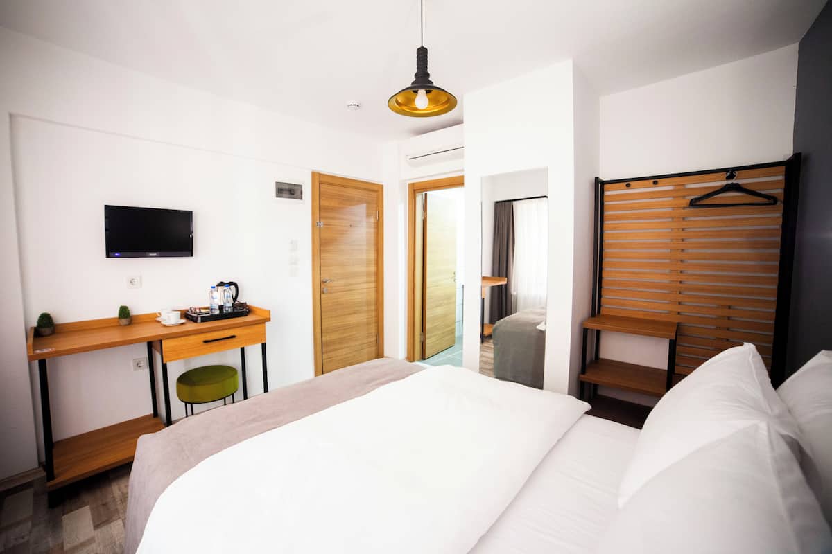 Habitación de hotel con cama, escritorio con silla, televisor, armario de madera y lámpara colgante.