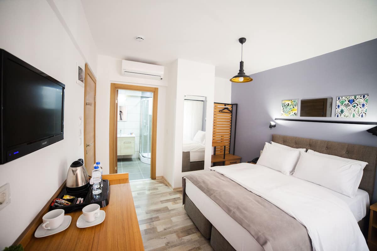 Una habitación de hotel con cama, televisor, escritorio con cafetera y tazas, y puerta que da a un baño.