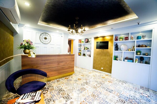 A hotel reception area with a wooden reception desk, a clock, and a chandelier. - Set Ozer Hotel (Çanakkale)