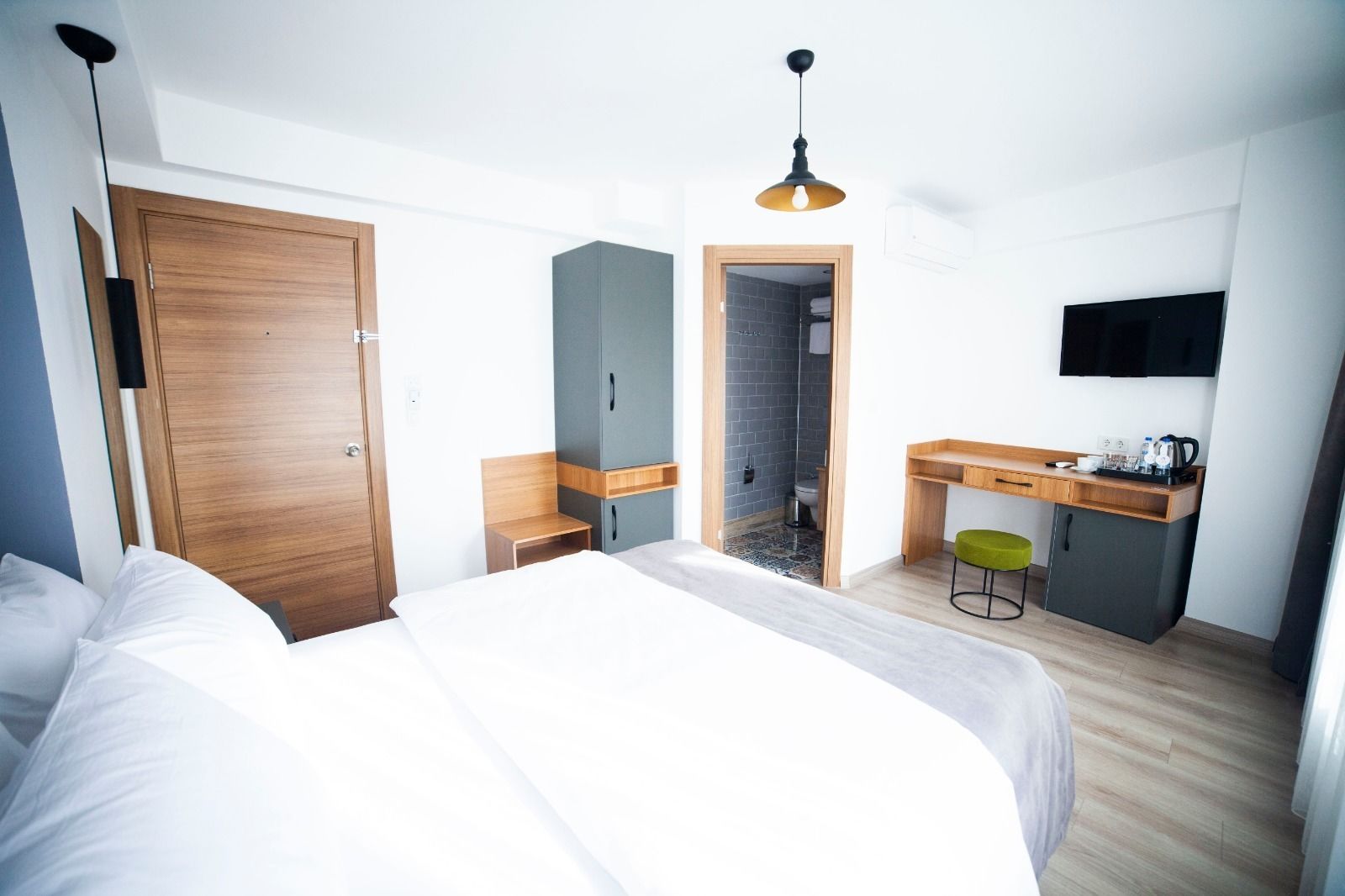 A modern hotel room with a large bed, a desk with a chair, a wardrobe, and a TV mounted on the wall.
