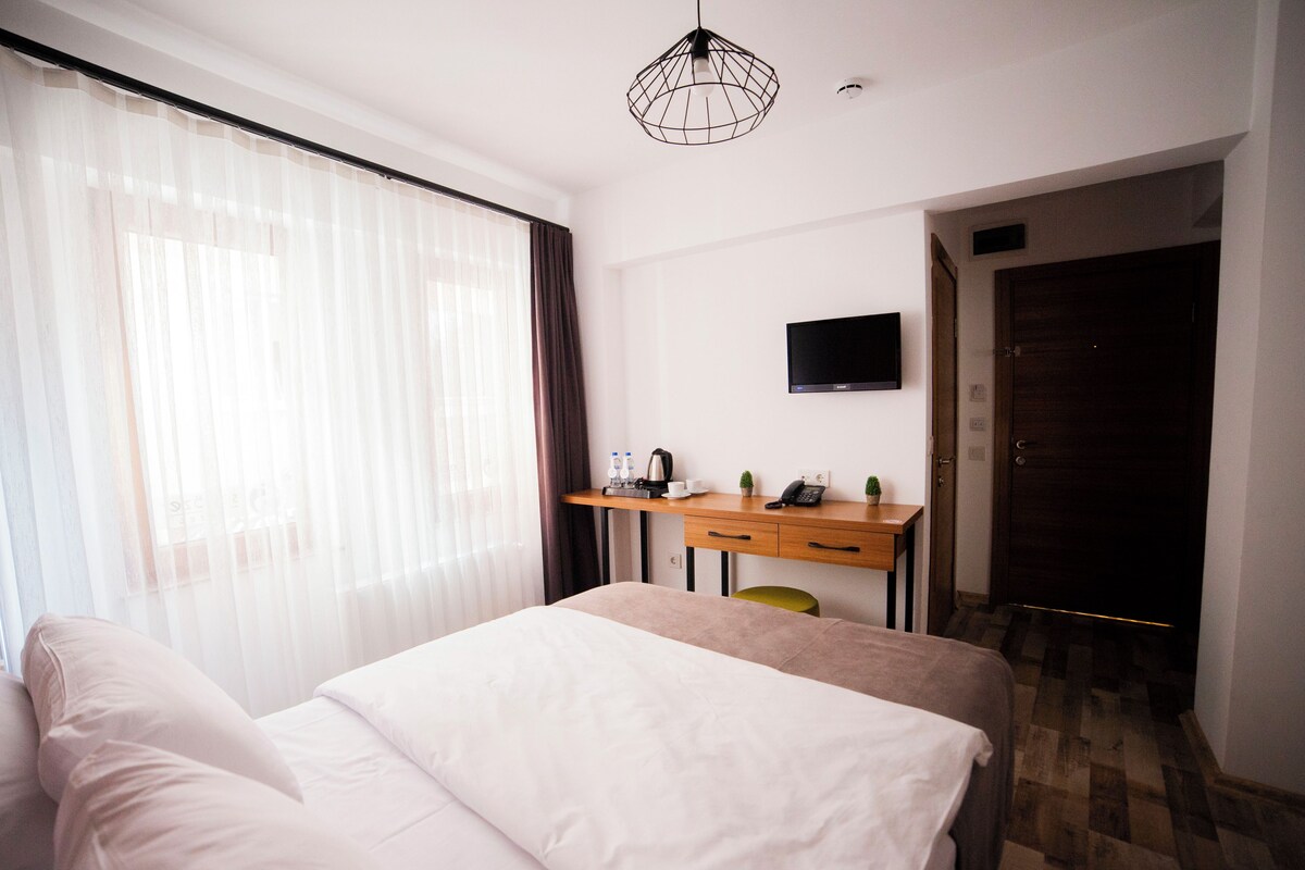 A hotel room with a bed, a desk with a computer, a TV, and a door.