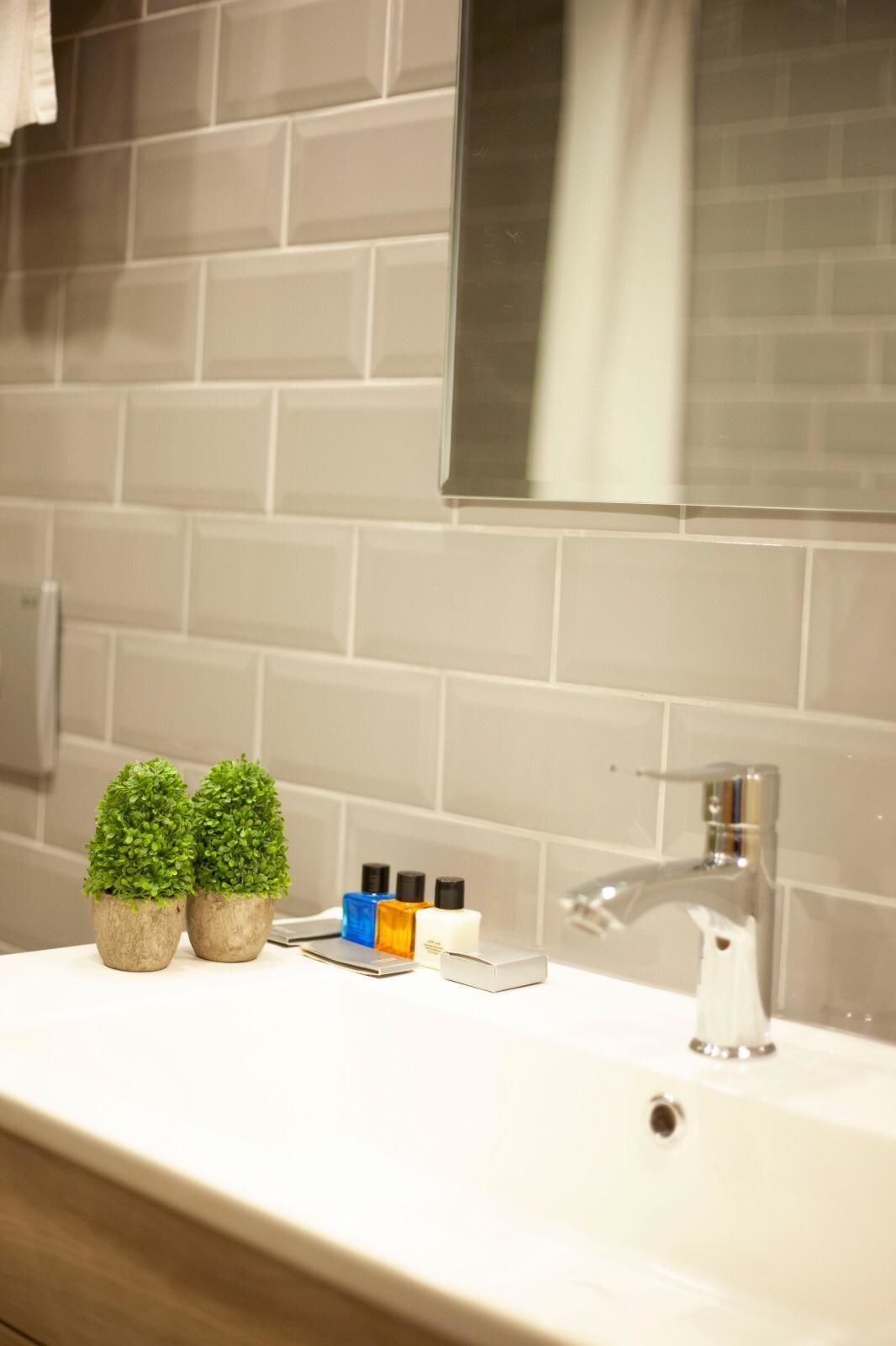 A bathroom with a white sink, two small potted plants, and toiletries on the counter.