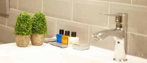 A bathroom with a white sink, two small potted plants, and toiletries on the counter.