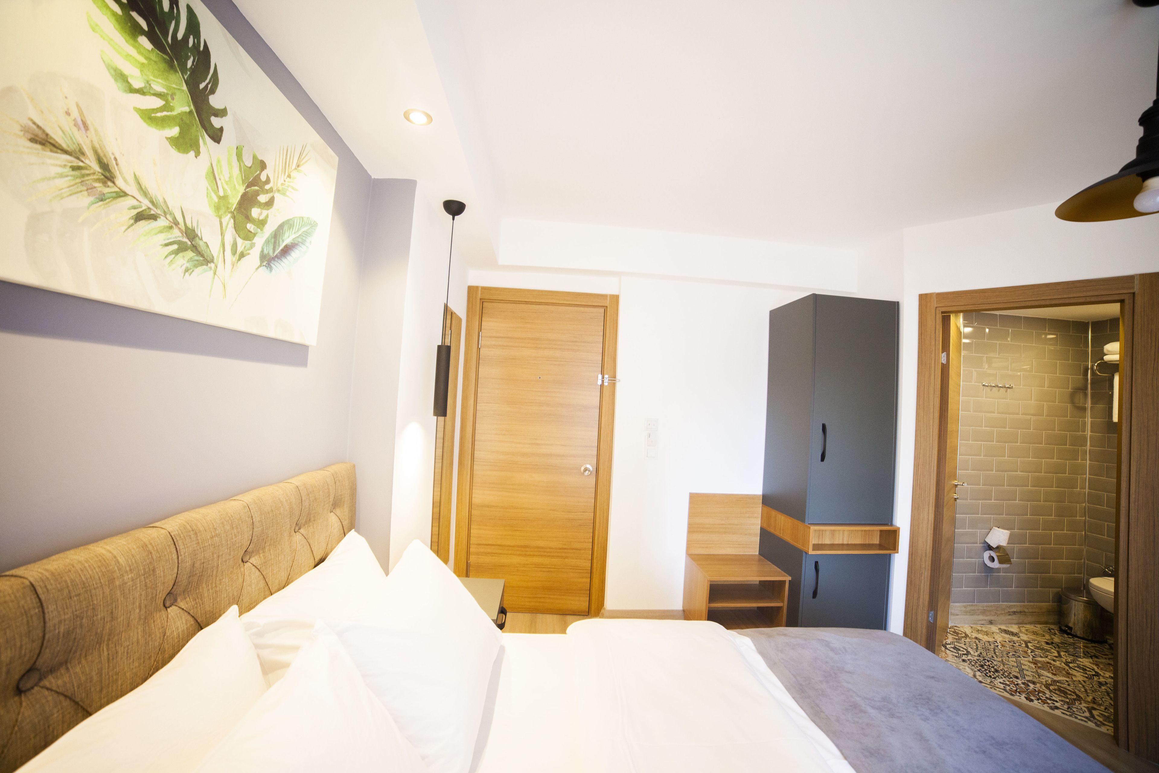A bedroom with a bed, a wooden headboard, a wooden door, a small table, and a shower area with a tiled wall.
