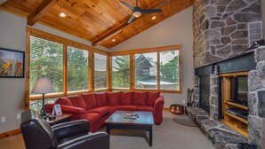 A cozy living room with a stone fireplace, a red sectional sofa, a wooden ceiling, and large windows. - Retreat on Main Street 4 Bedroom Townhome (McHenry)