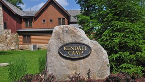 A large rock with a sign reading "Kendall Camp" in front of a wooden building with a stone foundation. - Retreat on Main Street 4 Bedroom Townhome (McHenry)