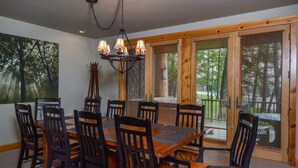 A dining room with a large wooden table and chairs, a chandelier, and large windows with blinds. - Retreat on Main Street 4 Bedroom Townhome (McHenry)