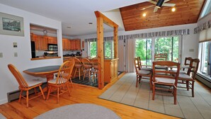 A spacious kitchen with wooden cabinets, a dining area with chairs, and a large window providing a view of greenery. - Sunrise 4 Bedroom House (Oakland)