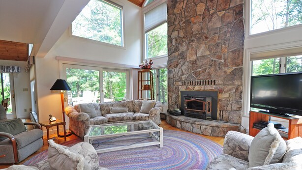 A spacious living room with a stone fireplace, large windows, and a flat-screen TV. - Sunrise 4 Bedroom House (Oakland)