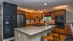 A modern kitchen with granite countertops, wooden cabinets, a stainless steel refrigerator, and a built-in oven. - Heavenly Grove 5 Bedroom House (Oakland)