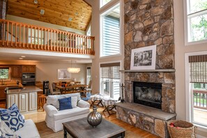 A spacious living area with a fireplace, wooden ceiling, and a stone accent wall. - Heavenly Grove 5 Bedroom House (Oakland)