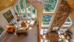 A spacious living room with a high ceiling, large windows, a stone accent wall, and a fireplace. - Heavenly Grove 5 Bedroom House (Oakland)