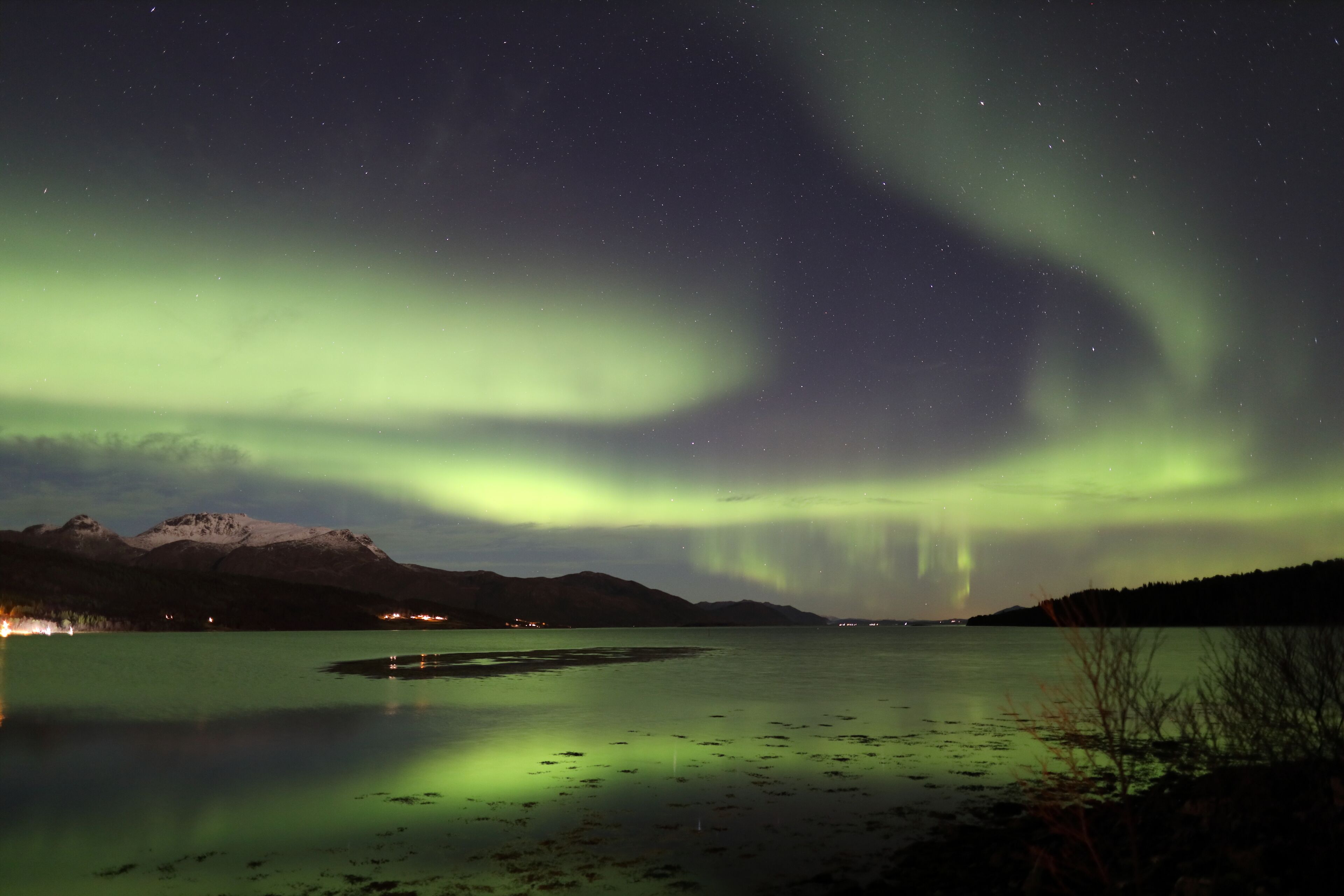 Vista nocturna de un lago con auroras boreales sobre montañas.