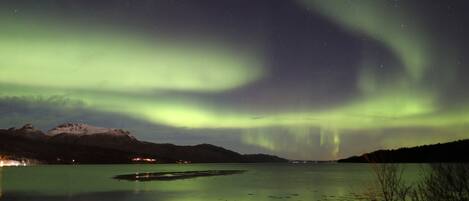Vista nocturna de un lago con auroras boreales sobre montañas.