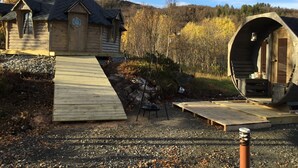 En træhytte med en rampe til en terrasse, omgivet af skov.