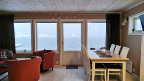 Et værelse med træloft, store vinduer med havudsigt, et spisebord med stole og en rød sofa.