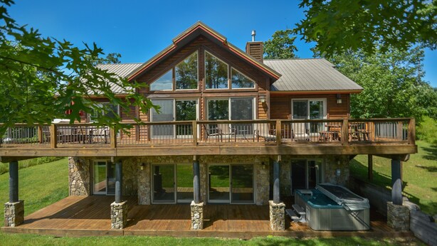 A two-story wooden house with a balcony, stone pillars, and a hot tub.