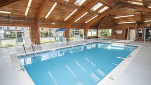 An indoor swimming pool with wooden beams, clear glass walls, and a blue pool. - Ski Harbor 4 Bedroom Townhome #30 (McHenry)
