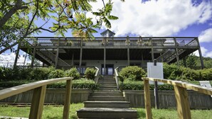 A wooden staircase leading to a covered deck with railings, surrounded by greenery.