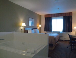 A hotel room with a large bathtub, a bed with pillows, two bedside lamps, a framed picture on the wall, and a window with curtains. - Quality Inn and Suites (yuma)