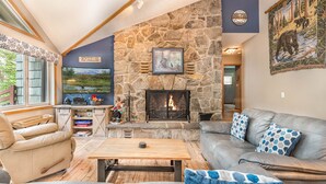 A cozy living room with a stone fireplace, leather sofas, and a large TV screen. - Brief Respite 5 Bedroom House (Swanton)