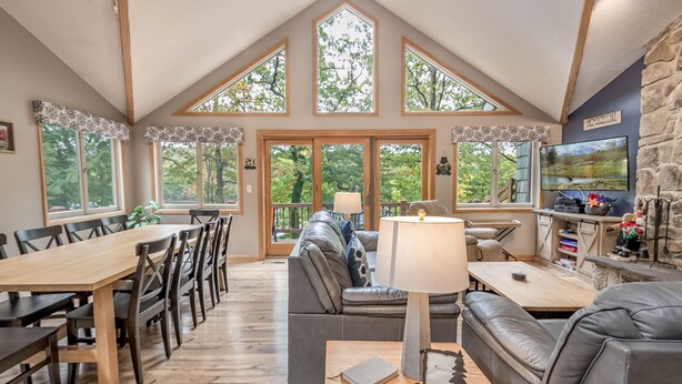 A spacious living area with a high ceiling, large windows, a fireplace, and a television. - Brief Respite 5 Bedroom House (Swanton)