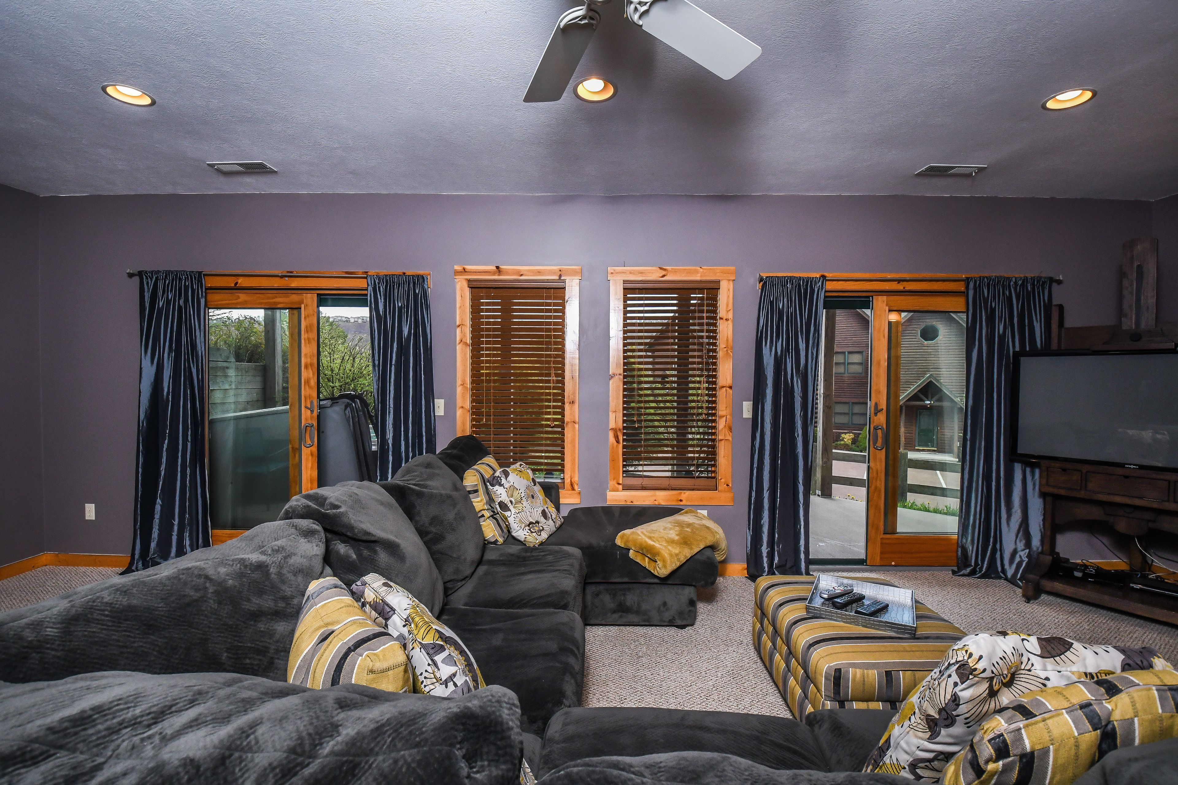 A living room with a sectional sofa, a TV, and a sliding glass door leading outside.