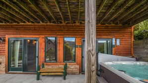 A wooden cabin with a hot tub, a bench, and a wooden post.