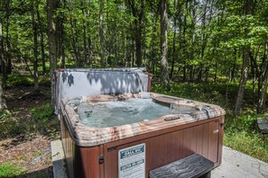 A hot tub in a wooded area with a safety sign.