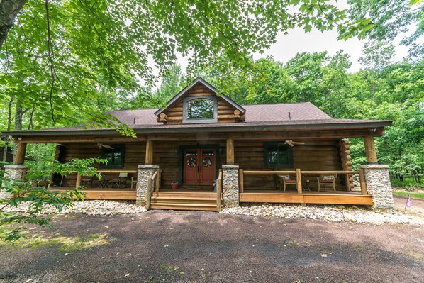 A log cabin with a front porch, stone pillars, and a wooden deck.