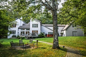 A large white house with a covered porch, a lawn with a bench, and a tree in the foreground. - Nature's Retreat 5 Bedroom House (Oakland)
