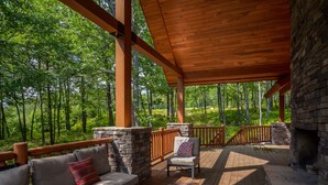Une terrasse couverte avec un plancher en bois, des piliers en pierre et une cheminée en pierre.