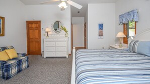 Een slaapkamer met een bed, een dressoir, een kaptafel, een plafondventilator, een deur en een raam met gordijnen.
