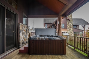 A hot tub on a wooden deck with stone walls and a covered area. - Big Sky 4 Bedroom Townhome (McHenry)
